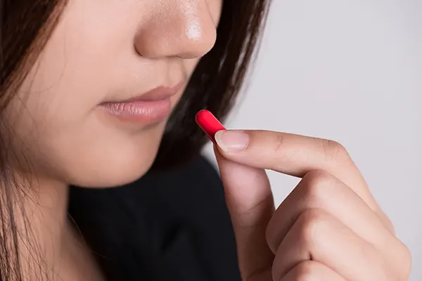 Oral Medication. A girl in her late teens is taking an isotretinoin pill for recurrent pimple breakouts